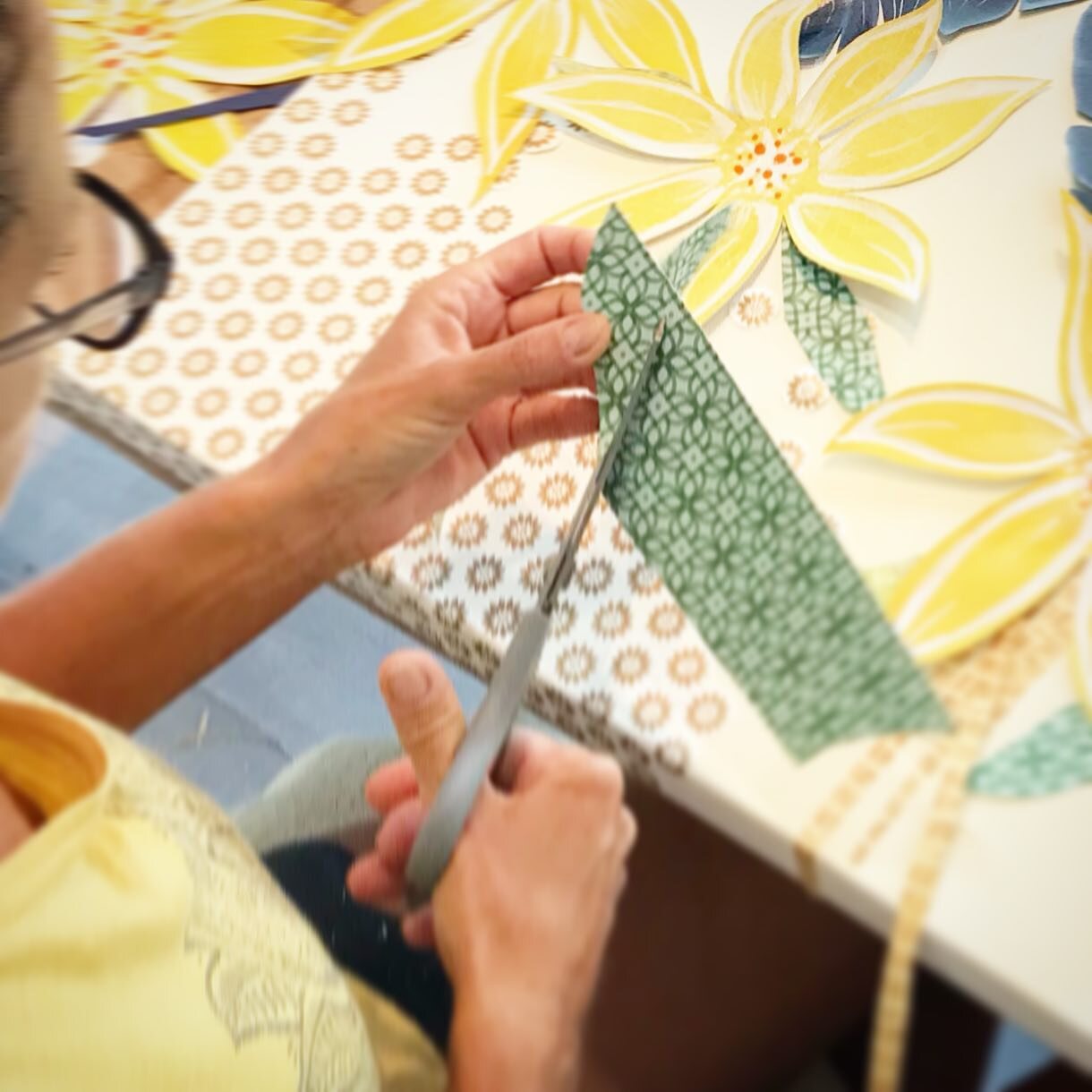 Hands cutting a leaf shape out of patterned green paper with scissors